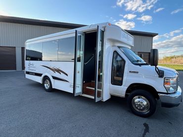 A white bus is parked in front of a building with its doors open.