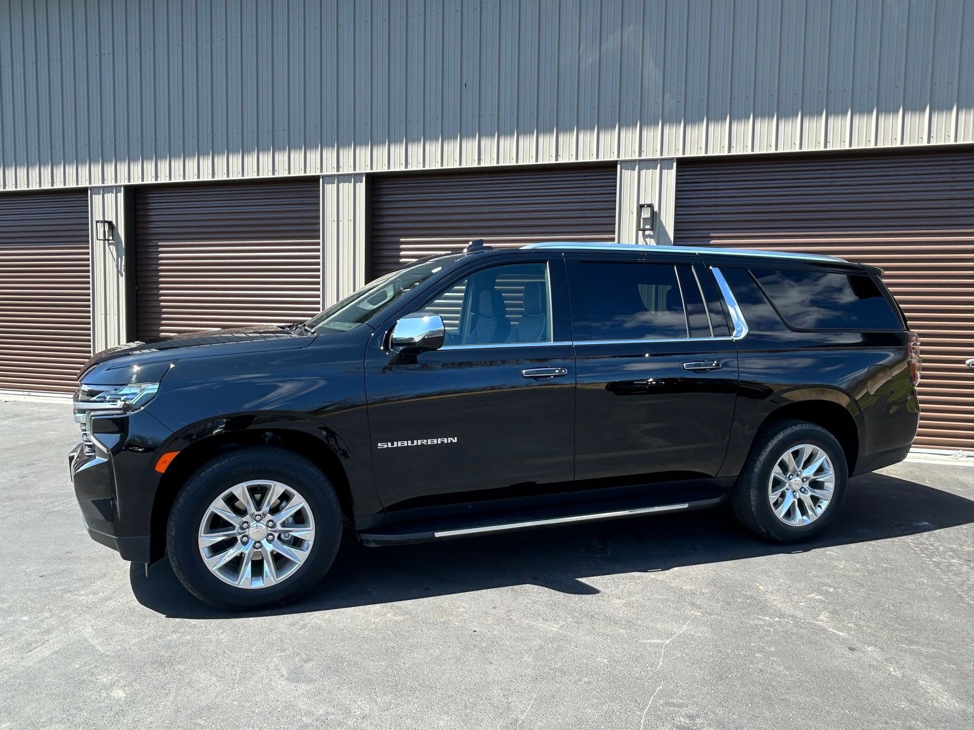 A side-profile view of a black SUV parked on asphalt in front of metal storage unit doors.