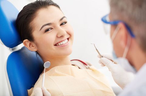 A woman is sitting in a dental chair while a dentist examines her teeth.