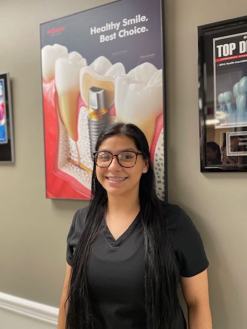 A woman wearing glasses and braces is standing in front of a dental poster.