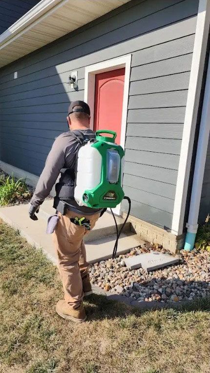 A man is spraying a house with a backpack sprayer.