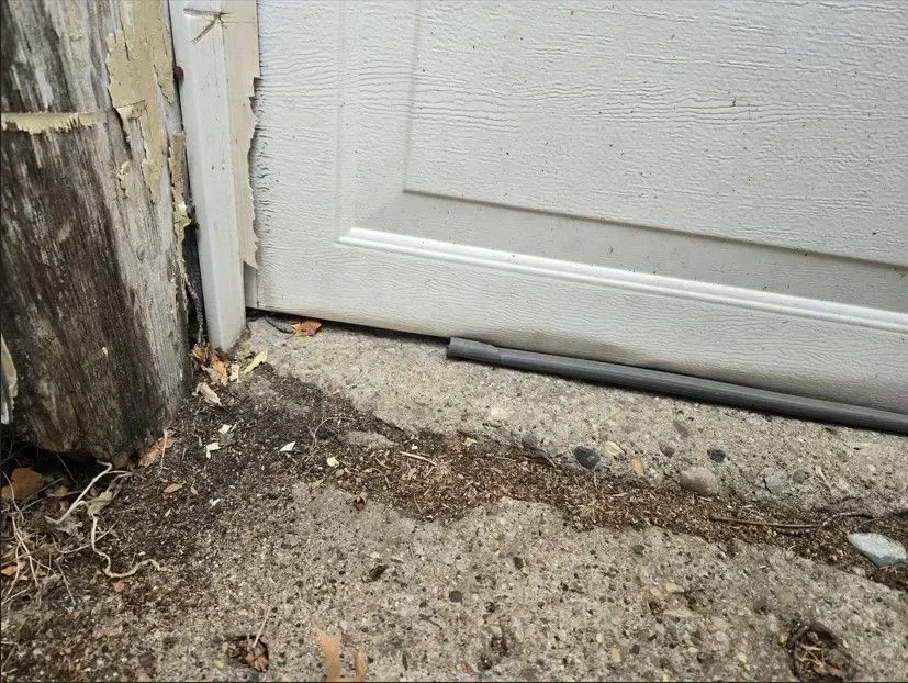 Garage door resting on concrete, debris and pipe in foreground.