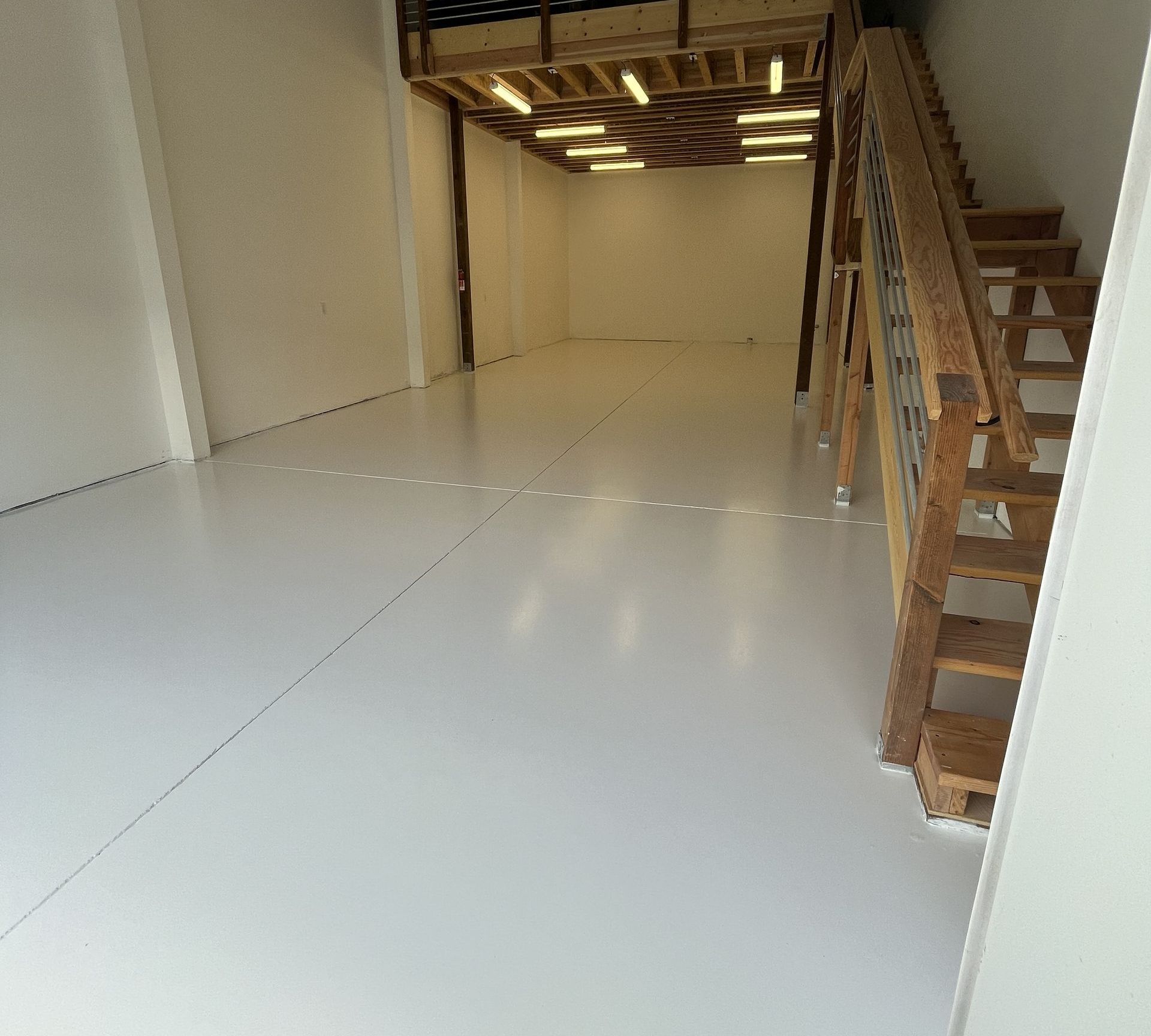 Empty, white-walled room with a wooden loft and staircase on the right. White floor; natural wood staircase.