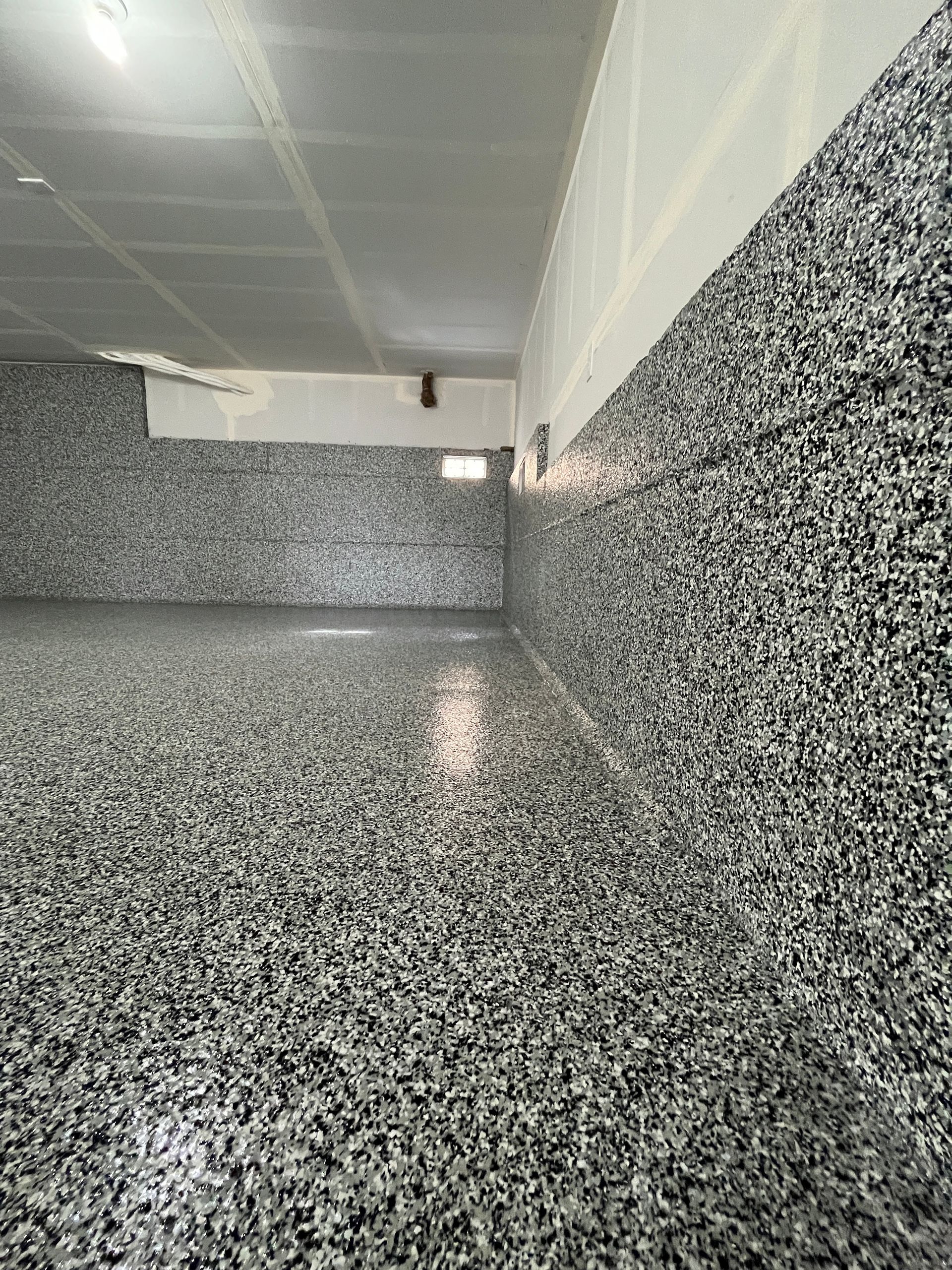 Garage interior with gray speckled epoxy floor and walls, white ceiling, and a small window.