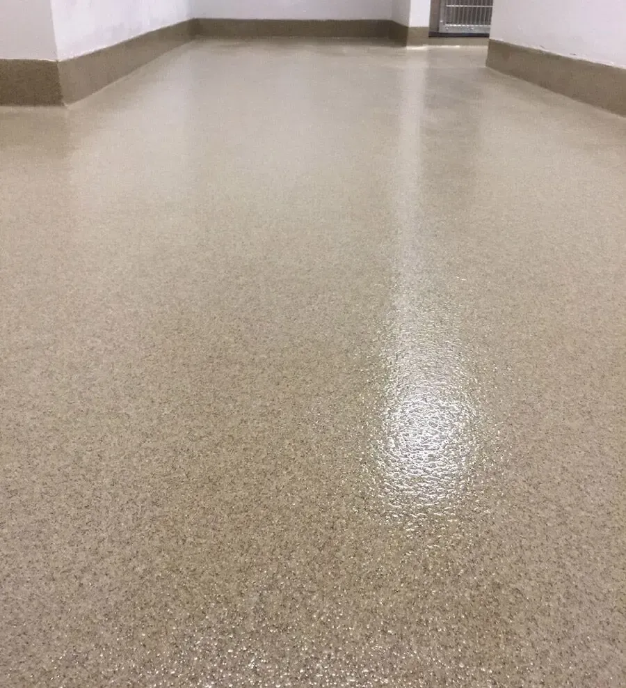 Tan epoxy-coated floor reflecting overhead light in a hallway. Beige walls and trim border the space.