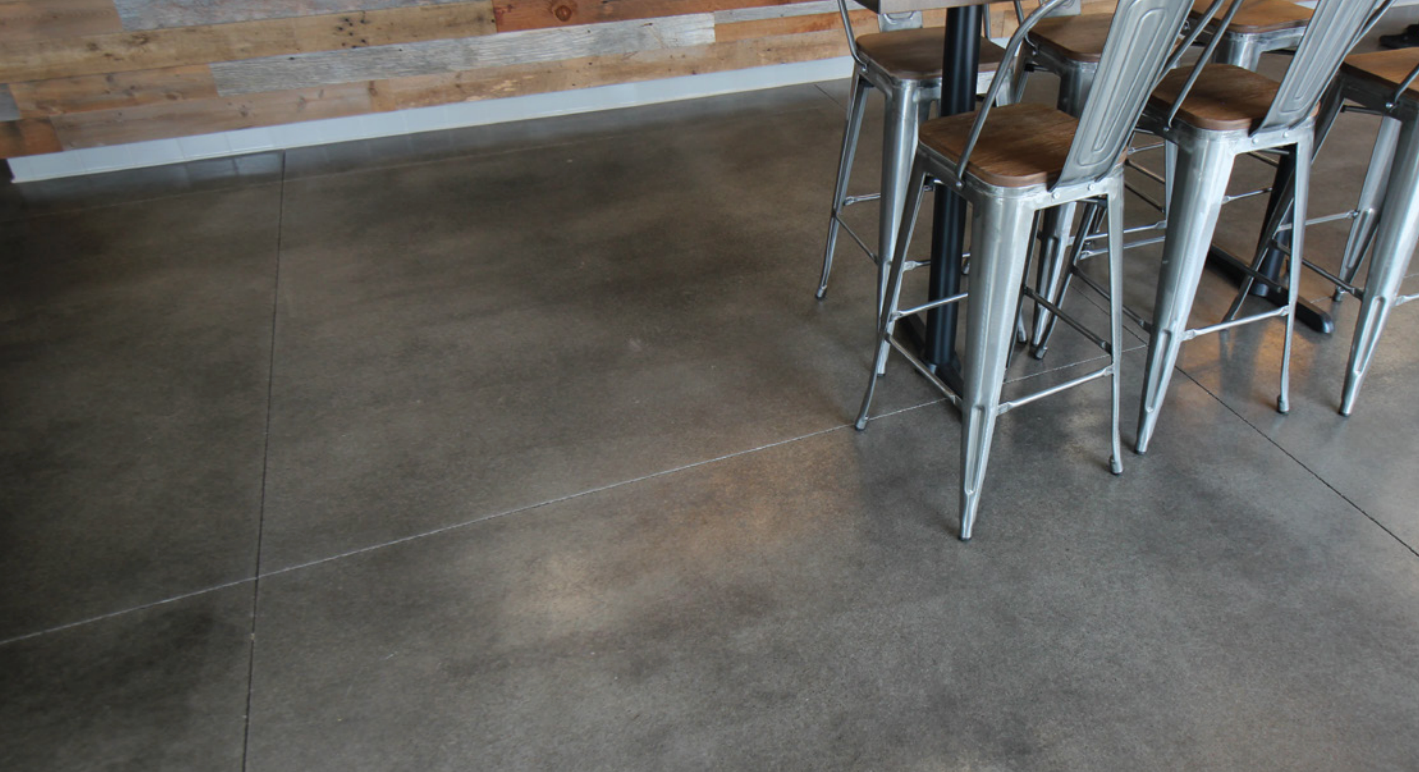 Gray concrete floor in a modern setting with metal bar stools and a wooden table, next to a wooden plank wall.