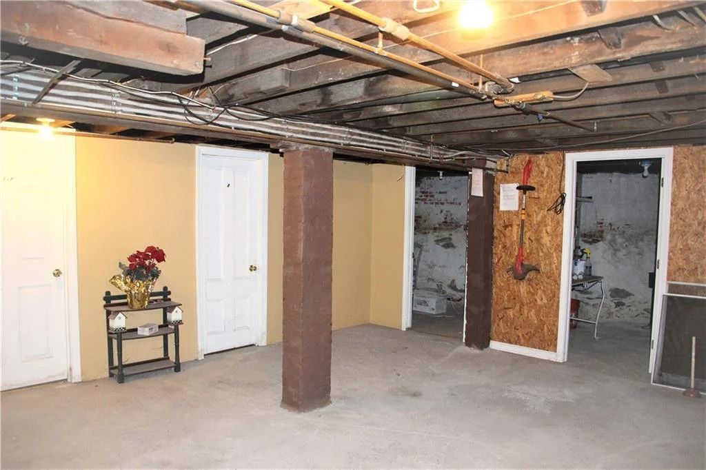 Basement with support beam, doors, and exposed ceiling with pipes. Concrete floor and painted walls.