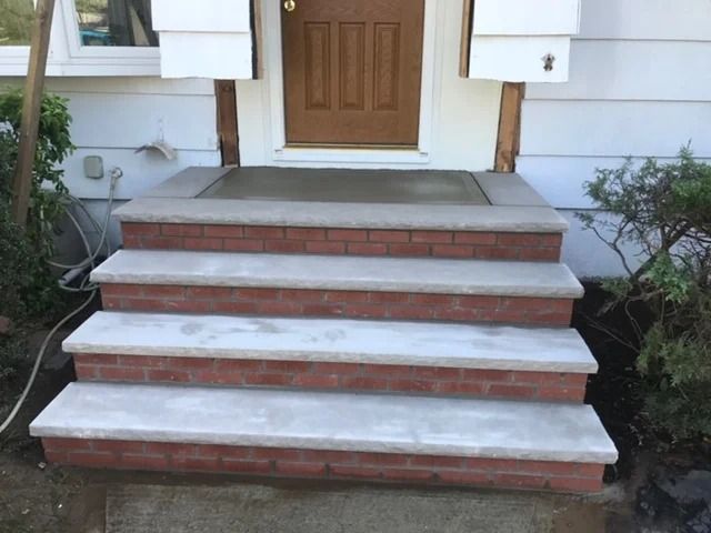 Brick and concrete front steps leading to a brown door; white siding and greenery are visible.