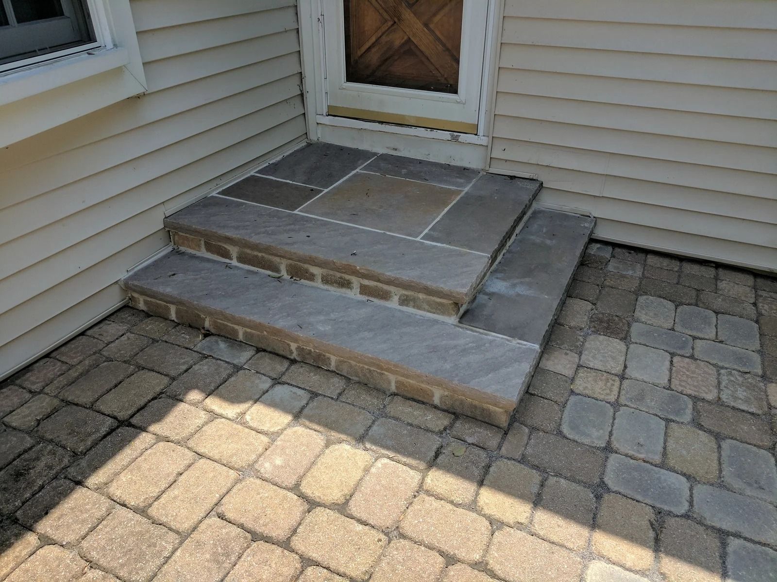 Stone steps leading to a wooden door, with a brick paver patio and siding.
