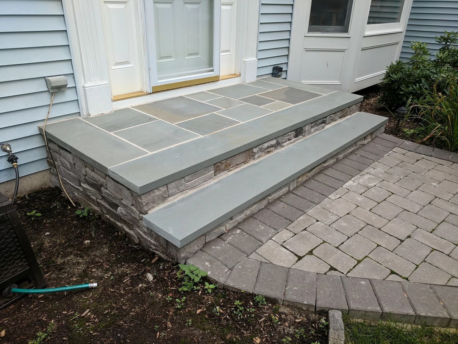 Stone steps leading up to a house entrance with a brick patio.