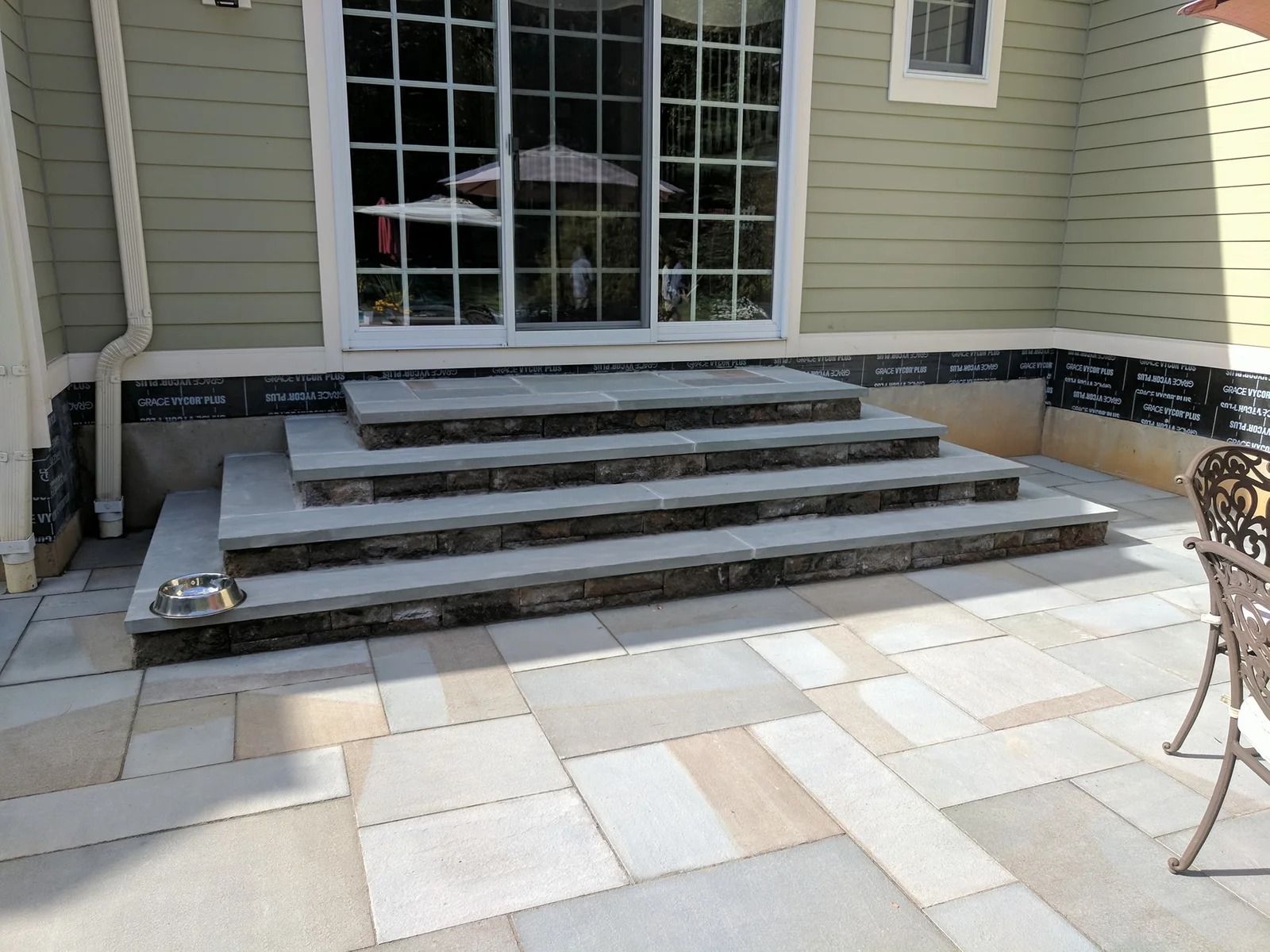 Stone steps leading to a sliding glass door on a patio with multi-toned stone pavers.