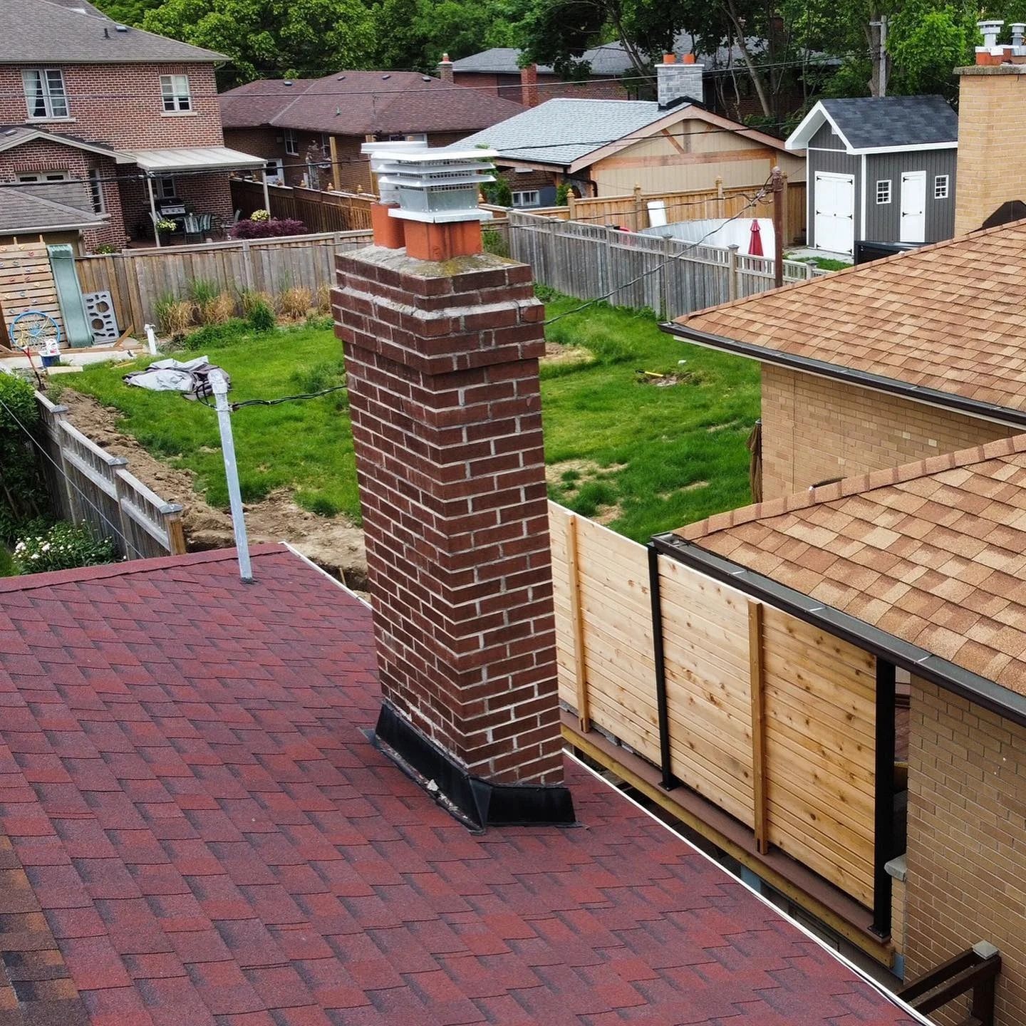 Brick chimney on a red-shingled roof. Houses and yards are visible in the background.