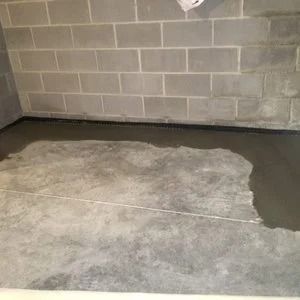 Concrete basement floor with water along one wall, gray cinder block wall.