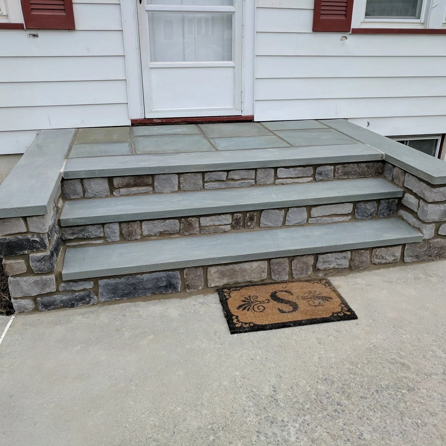 Stone steps leading to a white door with a welcome mat. The steps and stoop are blue-grey stone.