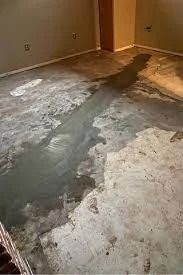 Concrete floor covered in water and discolored patches, possibly from a leak, in a room with light beige walls.