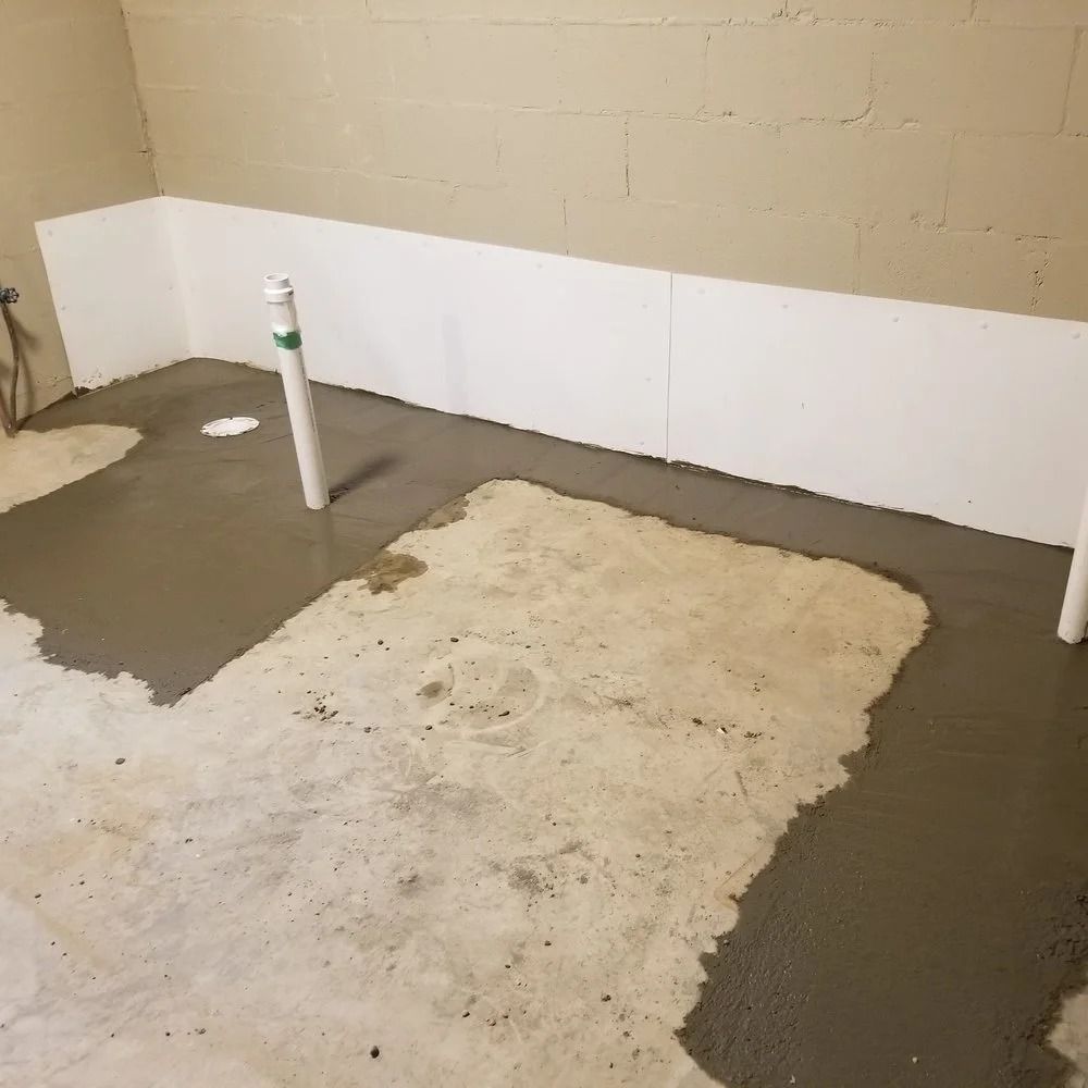 Basement with newly poured concrete floor, white wall panels, and plumbing pipes.