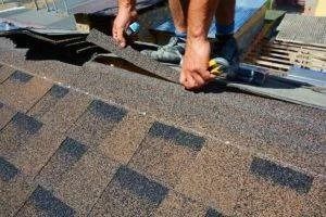 Person installing asphalt roof shingles on a brown roof.