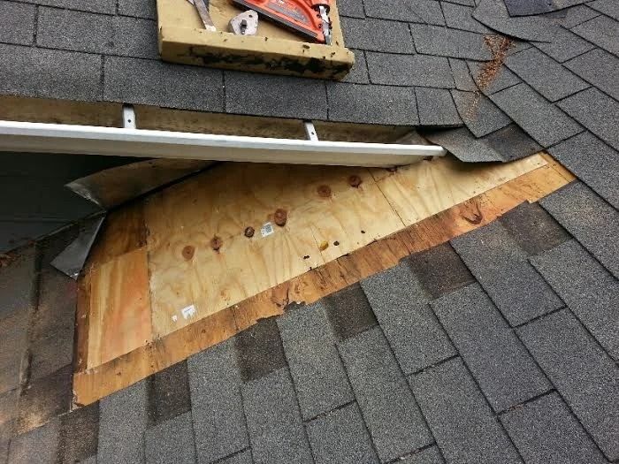Roof with exposed plywood repair and damaged asphalt shingles.