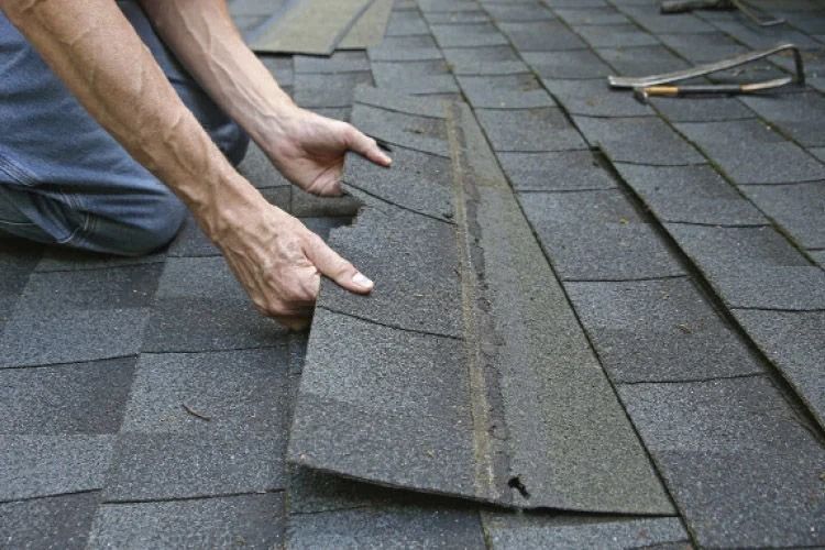 Person installing asphalt roof shingles, outdoors.