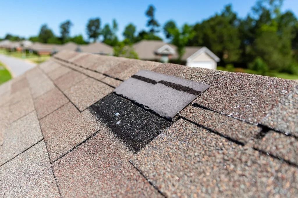Damaged roof shingles with missing and discolored sections, residential area in background.