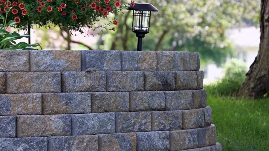 Stone retaining wall with solar lamp, red flowers, and green grass.
