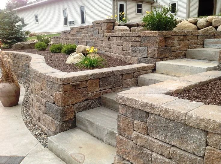 Stone retaining walls with steps and landscaping in front of a house.