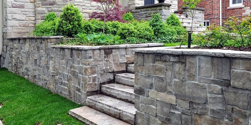 Stone retaining wall with steps, lush greenery, and a residential setting.