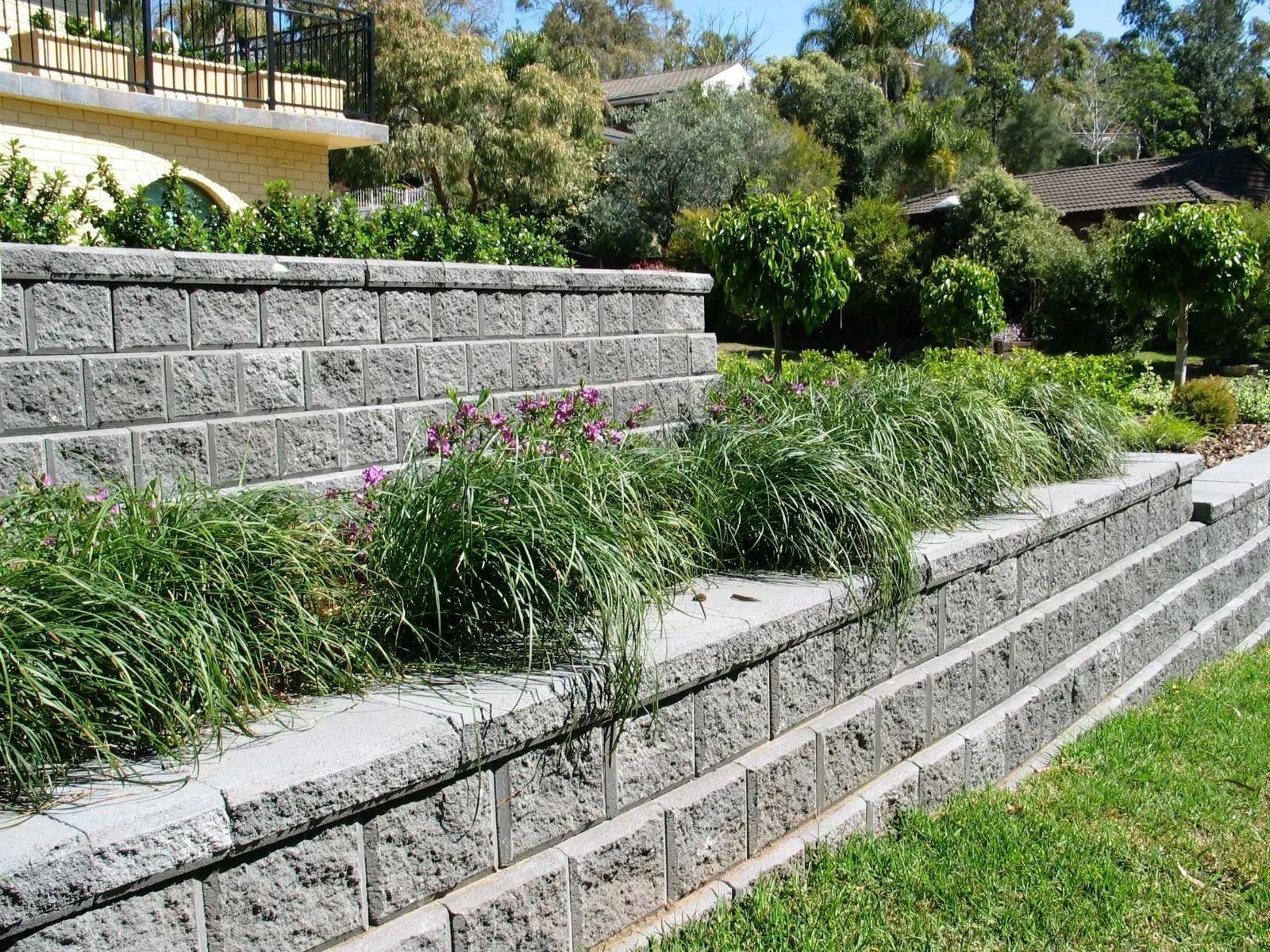 Gray block retaining walls with green grass and plants in a landscaped yard.