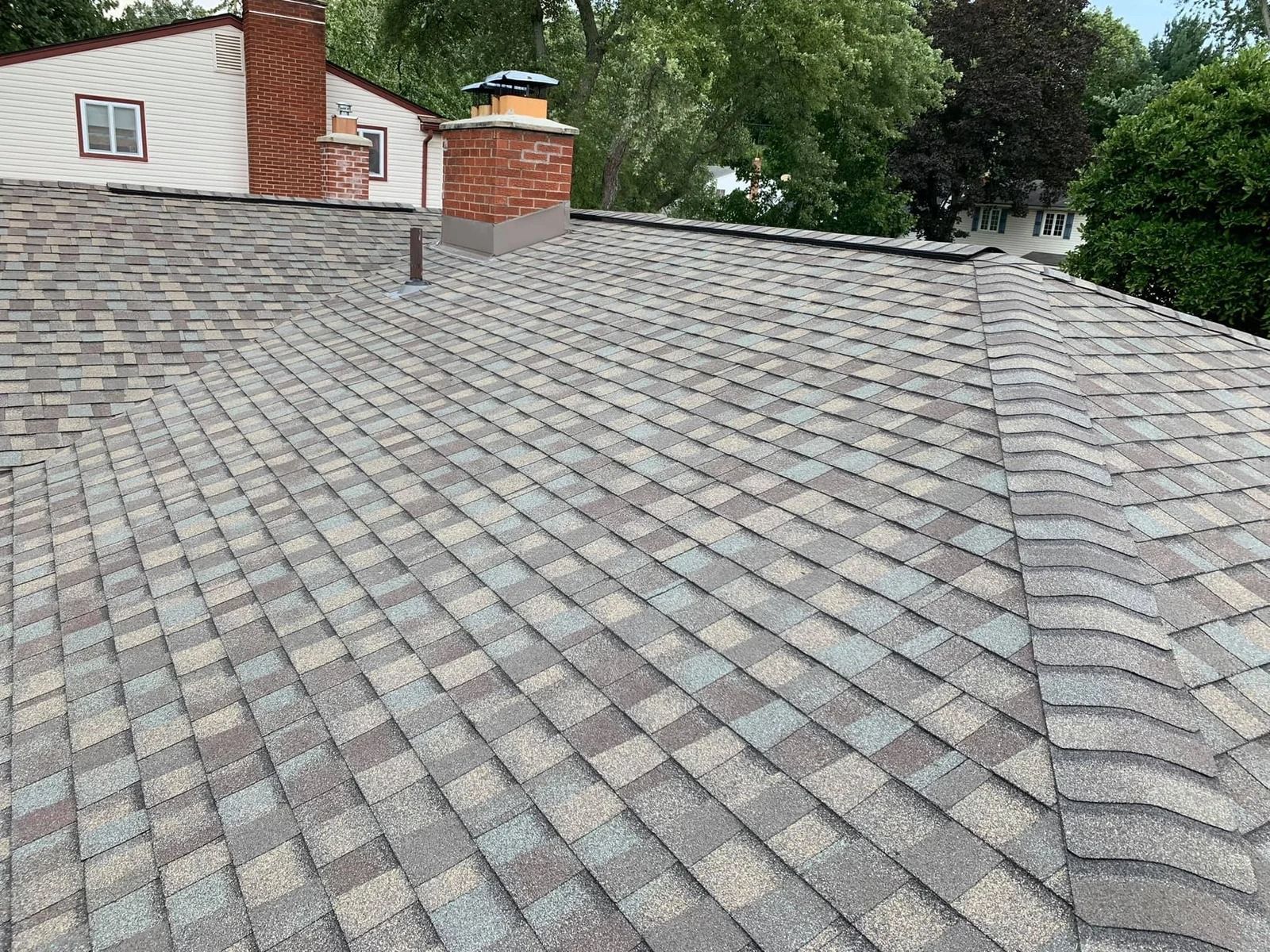 Overhead view of a roof with gray and brown asphalt shingles. A brick chimney is visible.