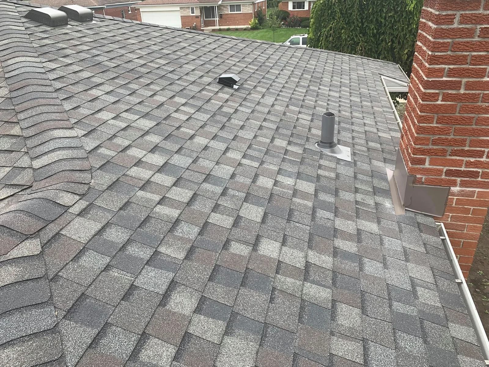 Gray and brown asphalt shingle roof with chimney and vents, angled view.