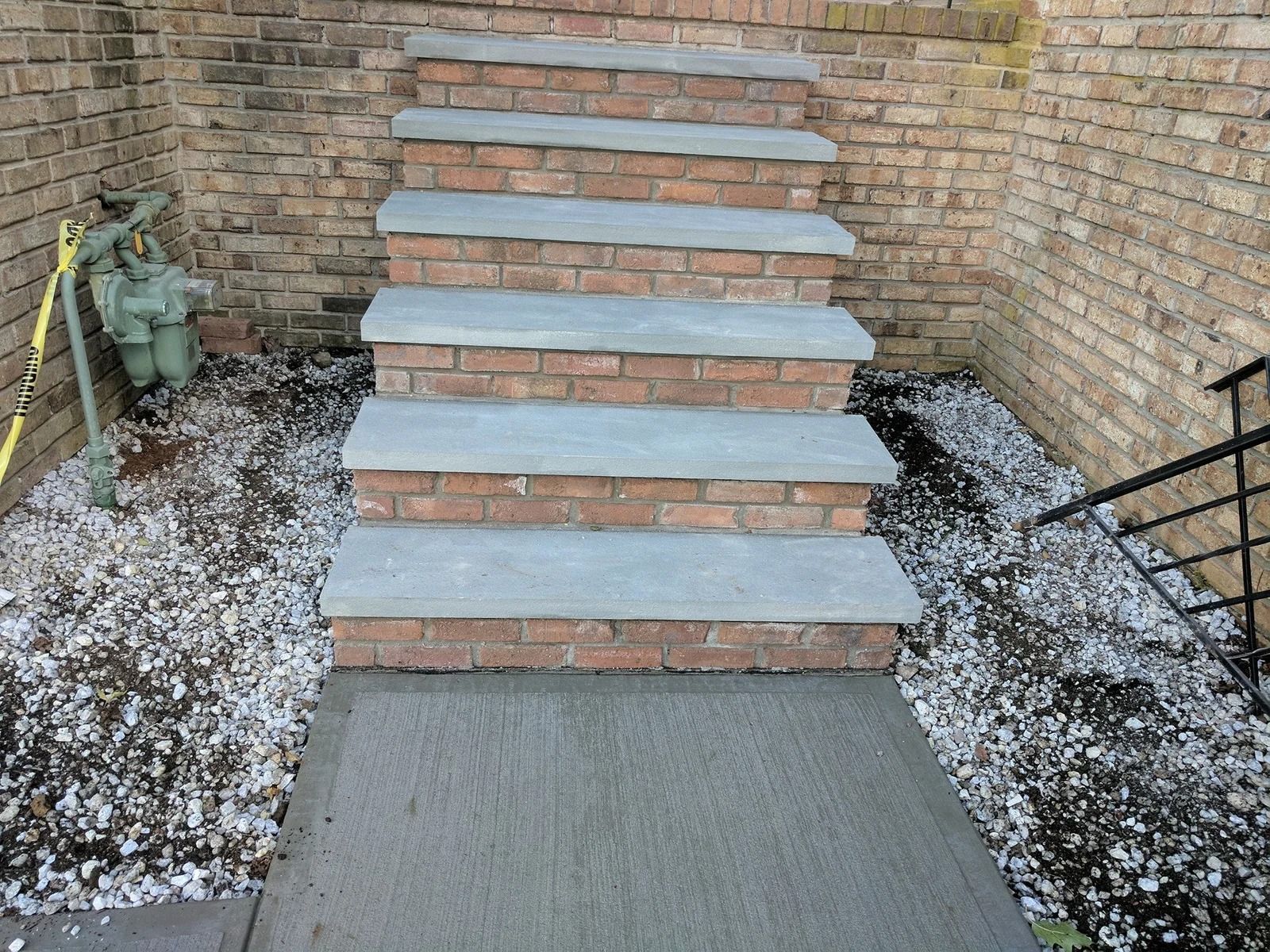Brick steps with stone treads leading up to a doorway, surrounded by gravel and a brick wall.