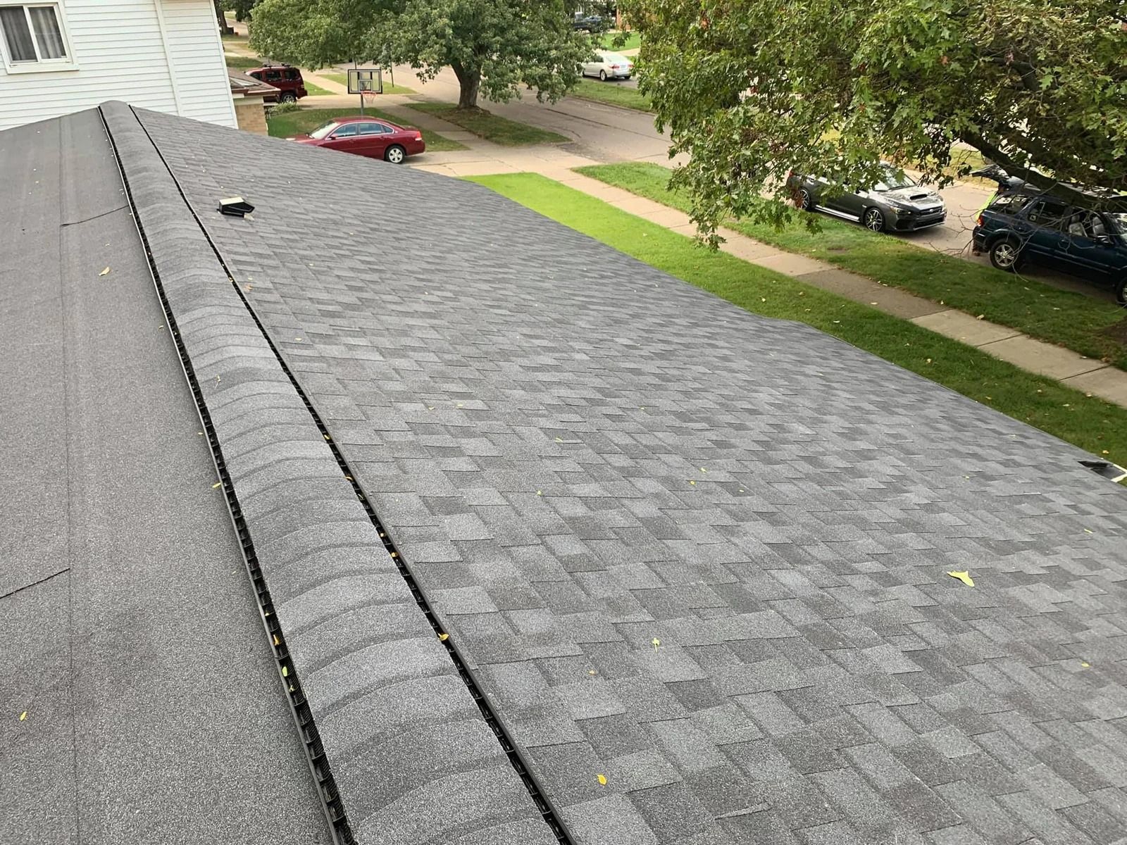 Gray shingle roof, angled view. A street with cars, grass, and trees are in the background.