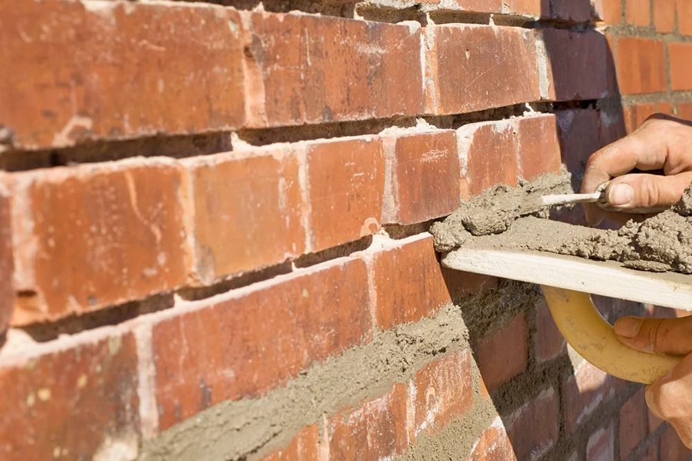Bricklayer using a trowel to apply mortar to a red brick wall.