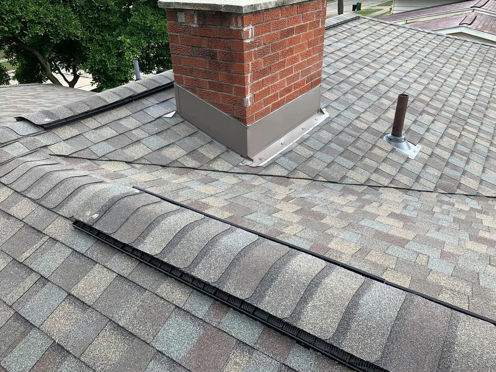 Roof with asphalt shingles and a brick chimney, with flashing and a vent pipe.