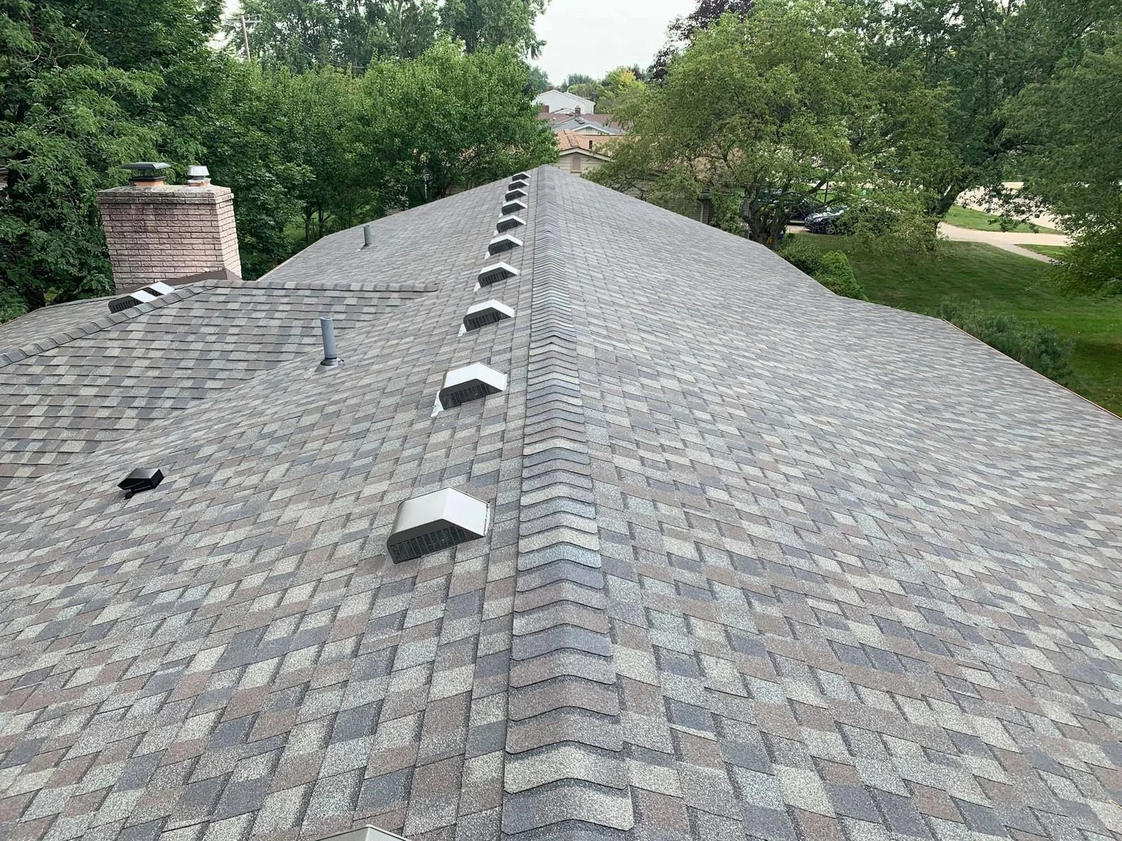 A roof covered in gray and brown shingles with several metal vent caps, trees in the background.