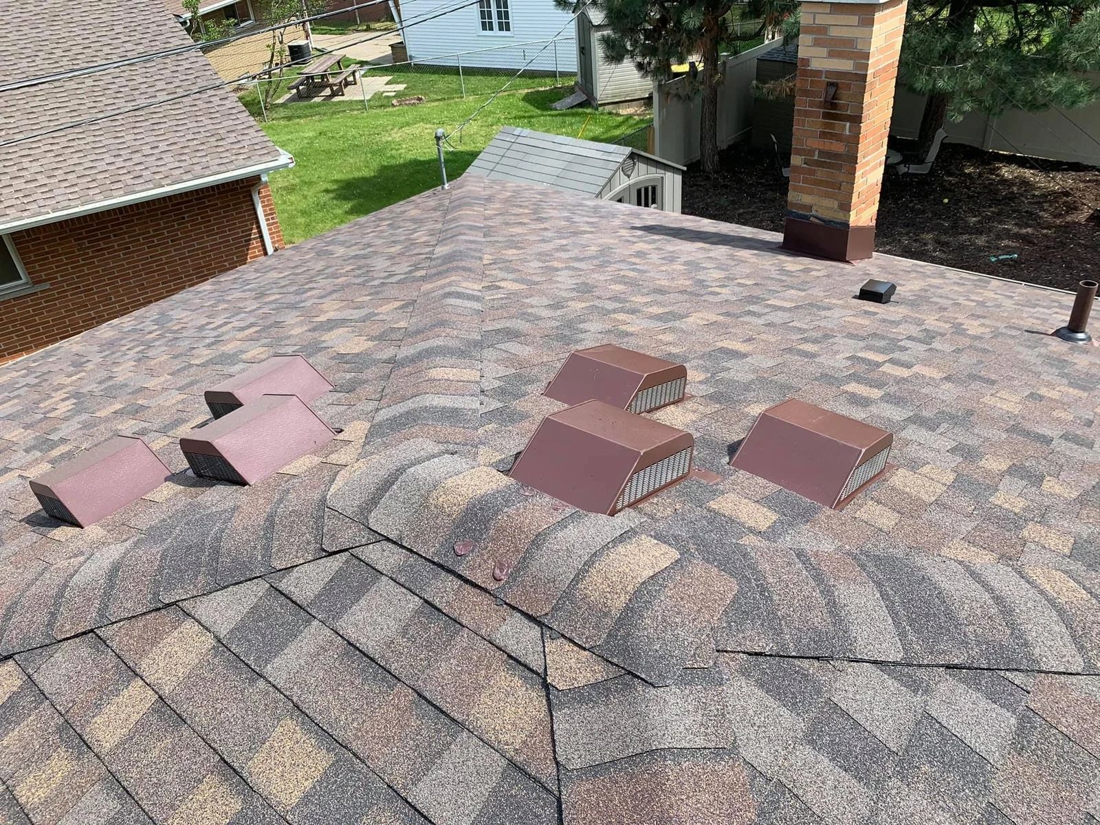 Rooftop with brown and tan shingles, several vents, and a brick chimney.