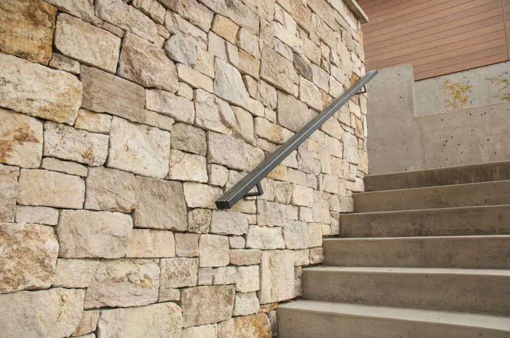 Stone wall with a handrail next to concrete stairs.