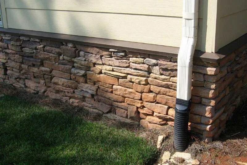 Stone facade on a house with a white downspout; green grass in front.