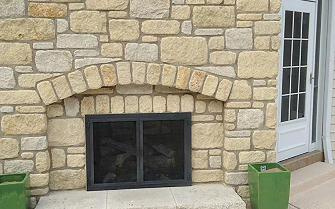 Stone fireplace with arched opening, black screen, and logs inside; cream-colored stone wall.