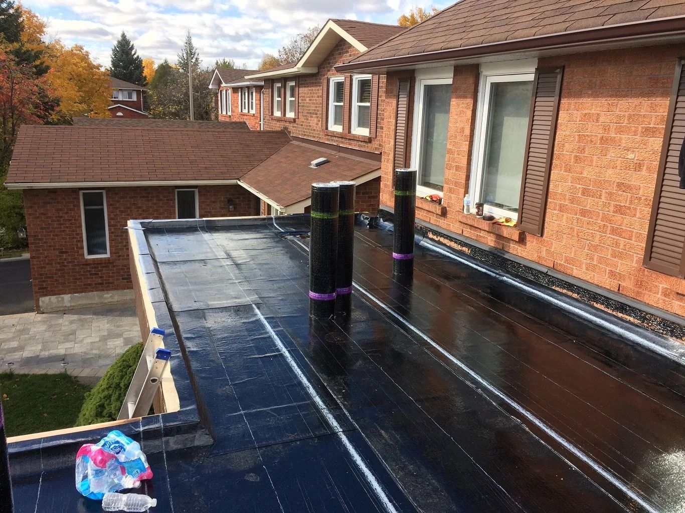 Black flat roof with ventilation pipes, brick buildings in background.