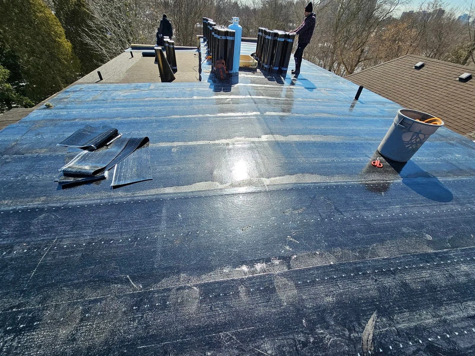 Workers installing a black flat roof, sunny outdoor setting.