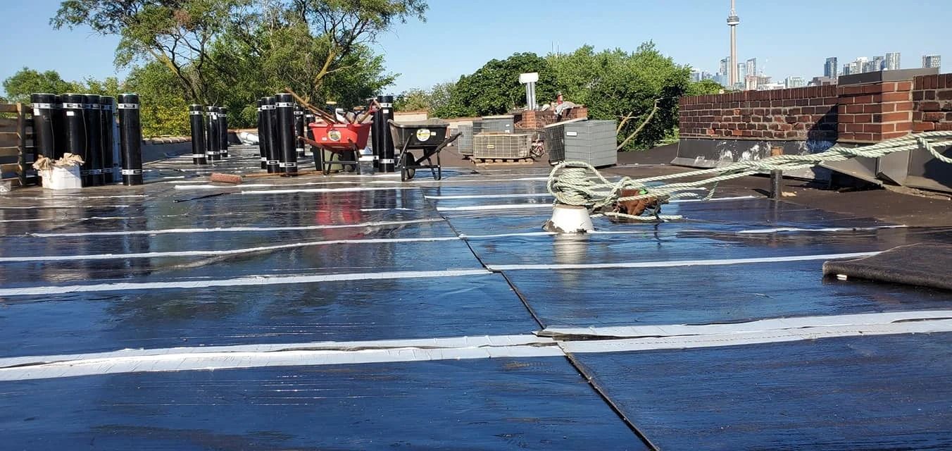 A flat roof with standing water, equipment, and a cityscape in the background.