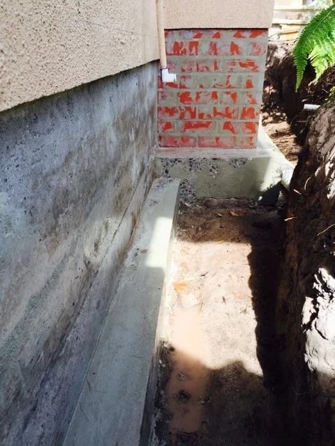 Concrete foundation and brick section of a building next to a trench, possibly for work.