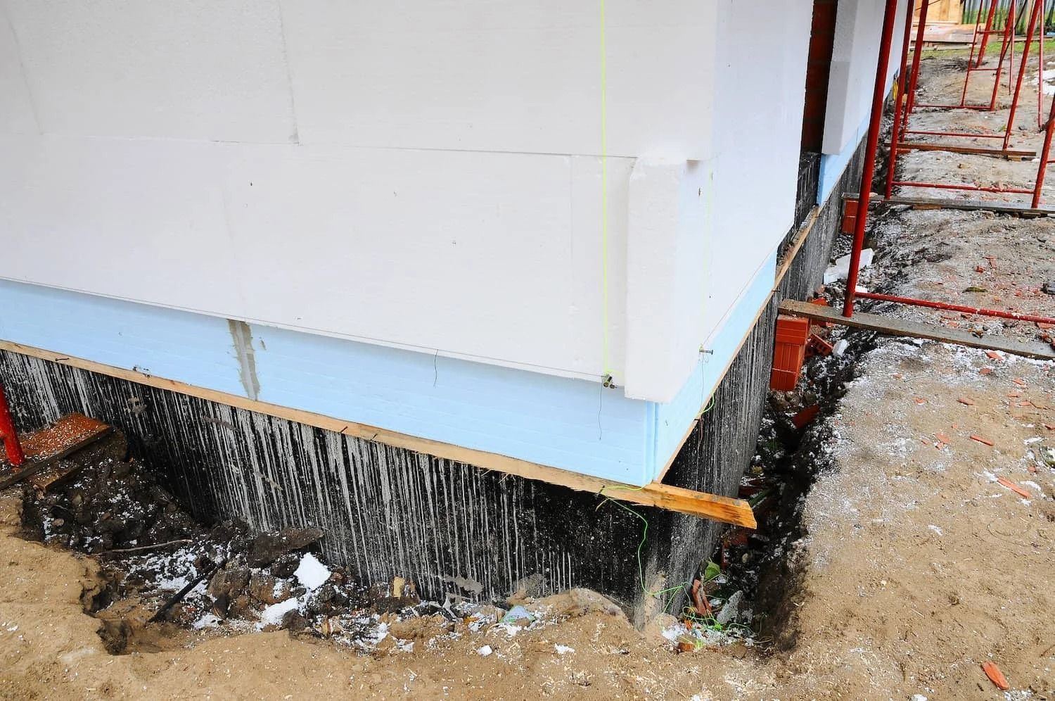 Corner of building under construction with blue insulation and exposed foundation.