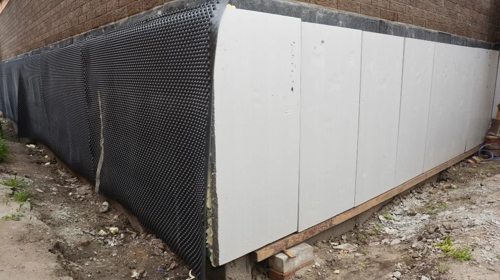 Exterior building corner with black drainage membrane and white paneling.