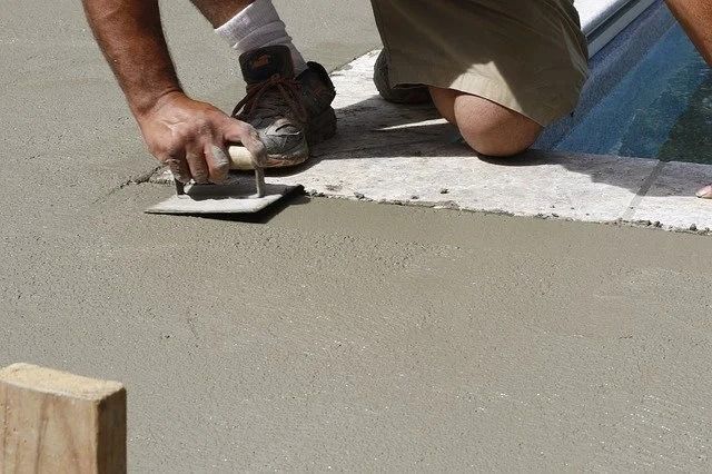 Person kneeling, using a trowel to smooth wet concrete.