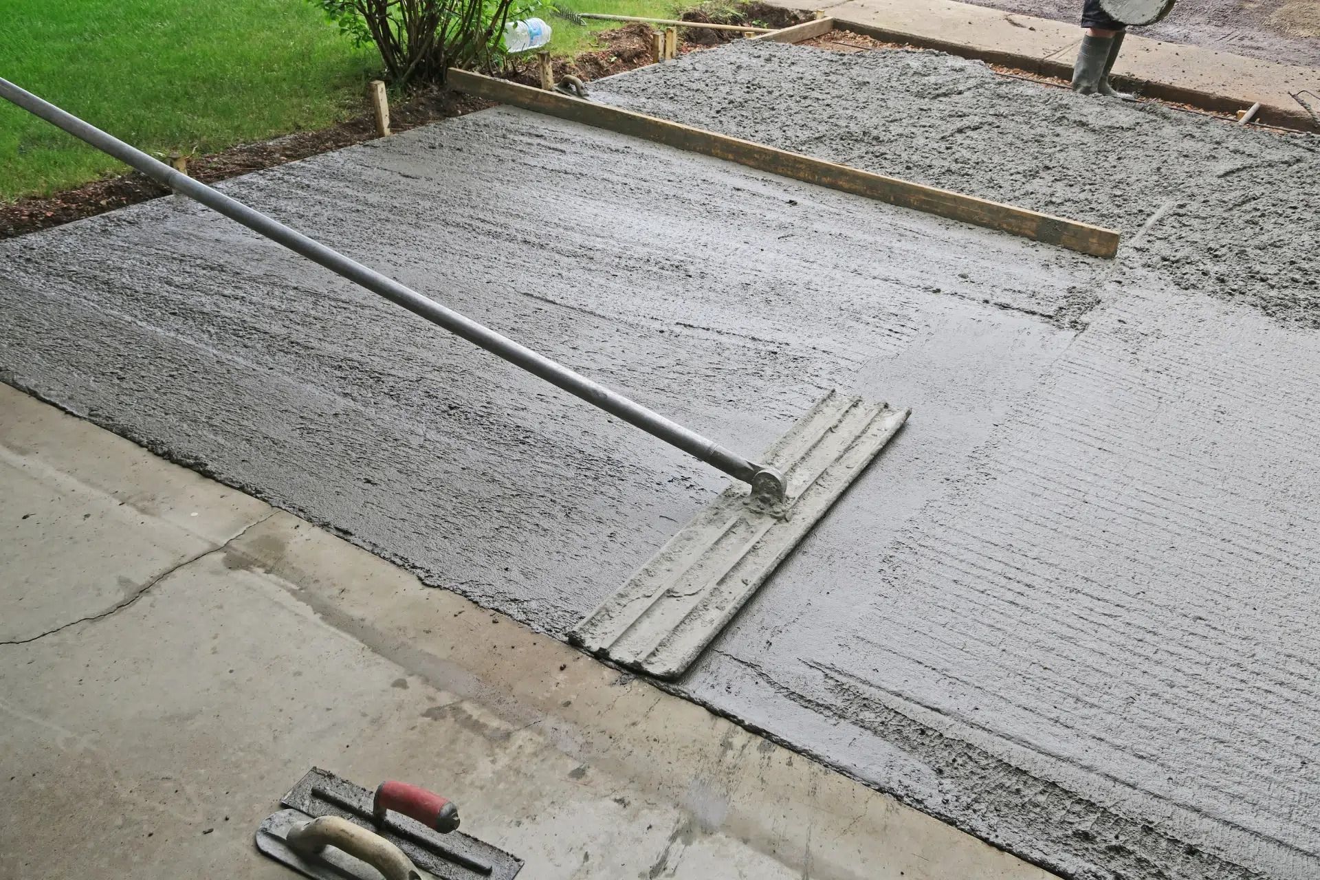 Fresh concrete being smoothed with a long-handled tool for a driveway or walkway.