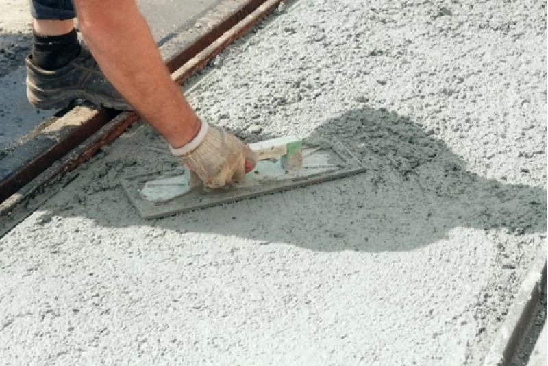 Person using a trowel to smooth wet concrete, alongside metal forms.