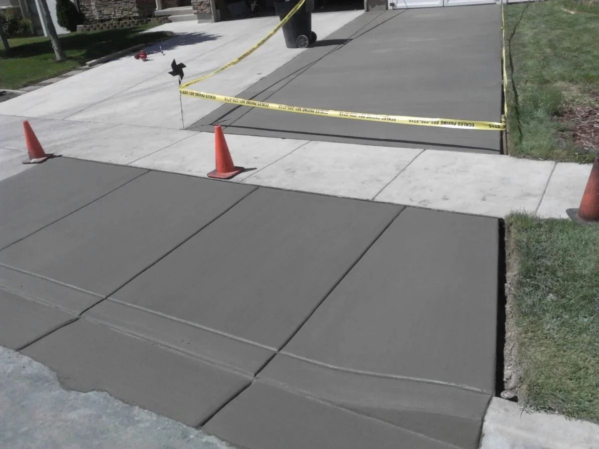 Freshly poured concrete driveway and sidewalk sections, bordered with caution tape and cones.