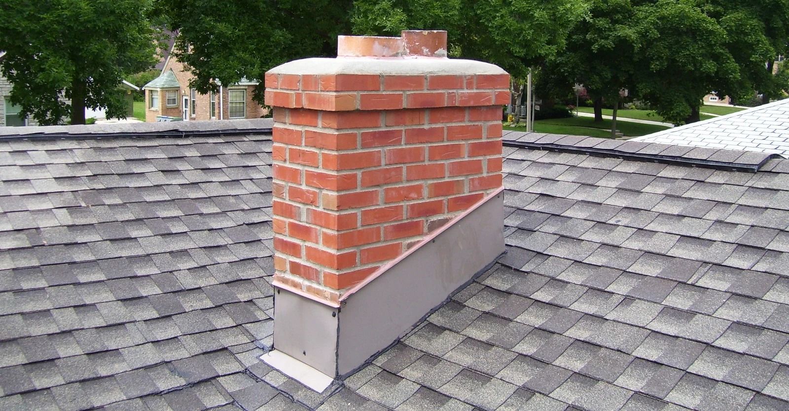 Brick chimney on a gray shingle roof, with metal flashing for water protection.